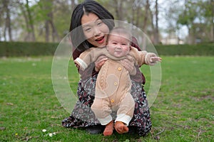 young happy and beautiful Asian Chinese woman holding little daughter, a cute an adorable baby girl, playful together in the park