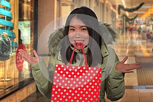 Young happy and beautiful Asian Chinese woman holding red shopping bag buying Christmas present in city mall smiling excited and