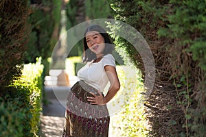 Young happy and beautiful Asian Chinese woman posing outdoors happy and cheerful at city park pregnant showing her belly proud