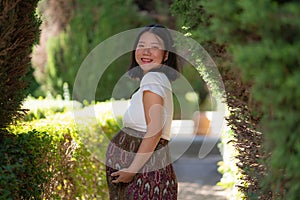 Young happy and beautiful Asian Chinese woman posing outdoors happy and cheerful at city park pregnant showing her belly proud