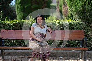 Young happy and beautiful Asian Chinese woman pregnant showing her belly proud and cheerful smiling at city park bench happy in