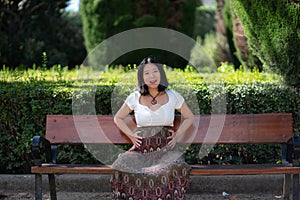 Young happy and beautiful Asian Chinese woman pregnant showing her belly proud and cheerful smiling at city park bench happy in