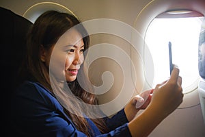 Young happy and beautiful Asian Chinese woman traveling for business inside airplane cabin smiling cheerful using mobile phone