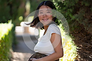 Young happy and beautiful Asian Japanese woman posing outdoors happy and cheerful at city park pregnant showing her belly proud