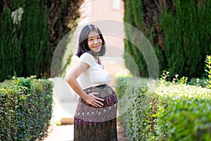 Young happy and beautiful Asian Japanese woman posing outdoors happy and cheerful at city park pregnant showing her belly proud