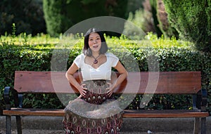 Young happy and beautiful Asian Japanese woman pregnant showing her belly proud and cheerful smiling at city park bench happy in
