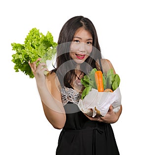 Young happy and beautiful Asian Korean woman holding bag full of vegetables smiling cheerful holding green lettuce in healthy