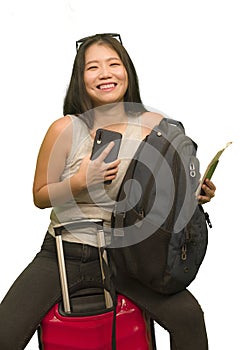 Young happy and beautiful Asian Korean woman carrying suitcase holding passport and mobile phone ready for holidays trip smiling