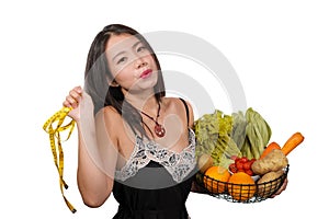 Young happy and beautiful Asian Korean woman holding basket full of vegetables and fruits smiling cheerful holding measure taylor