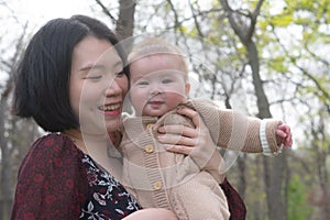 young happy and beautiful Asian Korean woman holding little daughter, a cute an adorable baby girl, playful together in the park