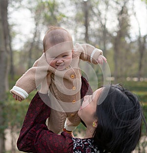 young happy and beautiful Asian Korean woman holding little daughter, a cute an adorable baby girl, playful together in the park