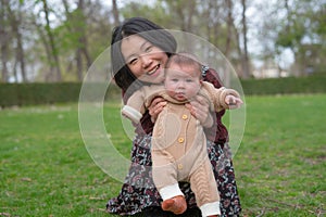 young happy and beautiful Asian Korean woman holding little daughter, a cute an adorable baby girl, playful together in the park