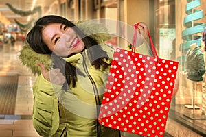 Young happy and beautiful Asian Korean woman holding red shopping bag buying Christmas present in city mall smiling excited and