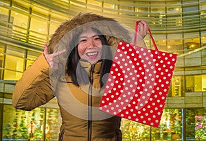 Young happy and beautiful Asian Korean woman holding shopping bag buying Christmas present in city mall smiling excited and