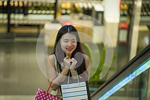 Young happy and beautiful Asian Korean woman at mall escalator carrying shopping bags in mall buying cheerful around fashion stor