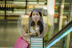 Young happy and beautiful Asian Korean woman at mall escalator carrying shopping bags in mall buying cheerful around fashion stor