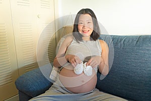 Young happy and beautiful Asian Korean woman pregnant on couch enjoying playful with little baby booties smiling relaxed at home