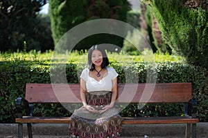 Young happy and beautiful Asian Korean woman pregnant showing her belly proud and cheerful smiling at city park bench happy in