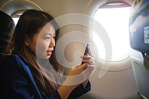 Young happy and beautiful Asian Korean woman traveling for business inside airplane cabin smiling cheerful using mobile phone in