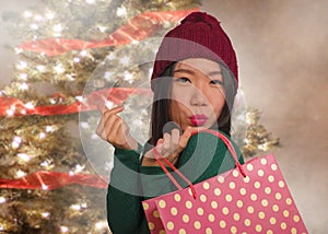 Young happy and beautiful Asian Korean woman in Winter hat holding shopping bag Christmas present excited and cheerful isolated on