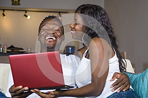 Young happy and beautiful black African American couple in love enjoying at living room sofa couch with laptop computer laughing