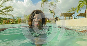 Happy and beautiful black African American woman in bikini having fun at tropical beach resort swimming pool relaxed and playful