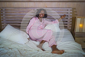 Young happy and beautiful black African American woman in pajamas lying relaxed and playful on bed smiling cheerful and positive