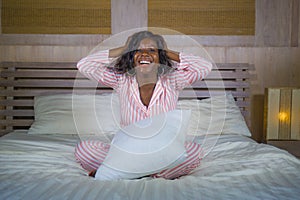 Young happy and beautiful black African American woman in pajamas lying relaxed and playful on bed smiling cheerful and positive