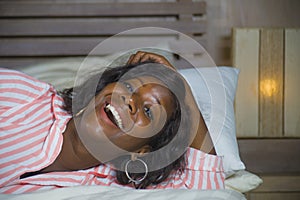 Young happy and beautiful black African American woman in pajamas lying relaxed and playful on bed smiling cheerful and positive