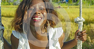 Young happy and beautiful black African American woman in Summer dress playing outdoors on swing smiling cheerful and relaxed