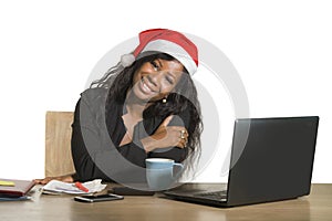 Young happy and beautiful black afro American business woman in Santa Christmas hat working at office computer desk smiling succes