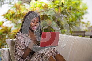 Young happy and beautiful black afro American woman in fashionable dress and working with laptop computer enjoying freelance