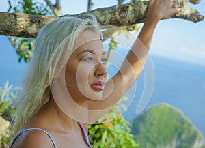 Young happy and beautiful blond woman relaxed feeling sea breeze at tropical beach cliff landscape enjoying Summer holidays