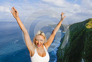 Young happy and beautiful blond woman smiling cheerful at tropical beach cliff landscape enjoying Summer holidays getaway carefree