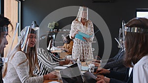 Young happy beautiful blonde female boss leading diverse business people team office meeting, all wearing face shields.