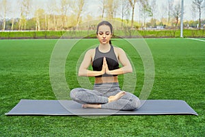 Young happy and beautiful brunette girl doing yoga workout in park, sitting in lotus pose meditating enjoying retreat in balance a