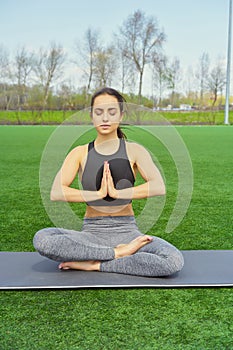 Young happy and beautiful brunette girl doing yoga workout in park, sitting in lotus pose meditating enjoying retreat in balance a