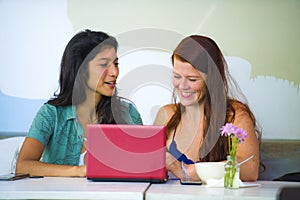 Young happy and beautiful caucasian and latin women working at office cafe with laptop computer discussing as digital business