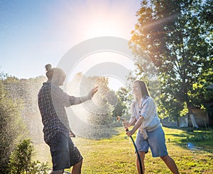 Young happy beautiful couple hosing in the garden, summer happiness and love concept, poured water from a garden hose of a spray