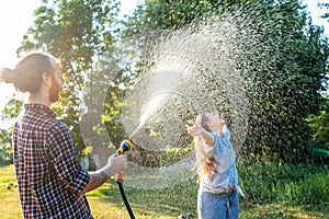 Young happy beautiful couple hosing in the garden, summer happiness and love concept, poured water from a garden hose of a spray