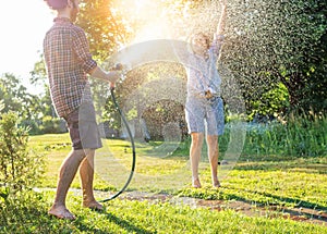 Young happy beautiful couple hosing in the garden, summer happiness and love concept, poured water from a garden hose of a spray