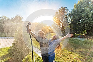 Young happy beautiful couple hosing in the garden, summer happiness and love concept, poured water from a garden hose of a spray