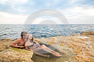 Young happy beautiful couple woman and man enjoying time in natural rock pool with water with rocks wall at background