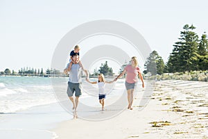 Young happy and beautiful family mother father holding hand of son and daughter walking joyful on the beach enjoying Summer holida