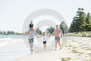 Young happy and beautiful family mother father holding hand of son and daughter walking joyful on the beach enjoying Summer holida