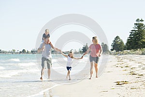 Young happy and beautiful family mother father holding hand of son and daughter walking joyful on the beach enjoying Summer holida