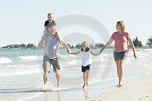 Young happy and beautiful family mother father holding hand of son and daughter walking joyful on the beach enjoying Summer holida