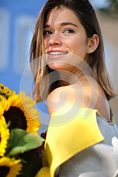 Young happy beautiful girl is walking in dress with a bouquet of sunflowers on a city street. Autumn concept