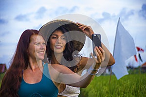 Young happy and beautiful hispanic girl in traditional Asian farmer hat and Caucasian woman taking girlfriends selfie together