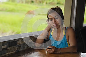 Young happy beautiful and serious Asian woman sitting in coffee shop using internet app on mobile phone pensive and thoughtful out